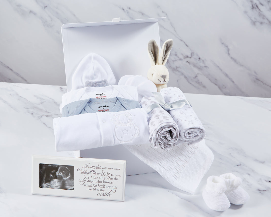 Unisex baby hamper, filled with 2 cotton baby vests, sleepsuit, bib, hat, 2 pairs of mittens, 2 cotton muslins, white cellular blanket, bunny toy, baby booties & photo frame. 